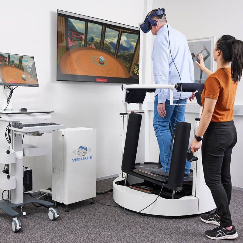 En audiolog hjælper en ældre mand med en balance- og genoptræningsøvelse med BalanceVR-udstyr på MotionVR-platformen.